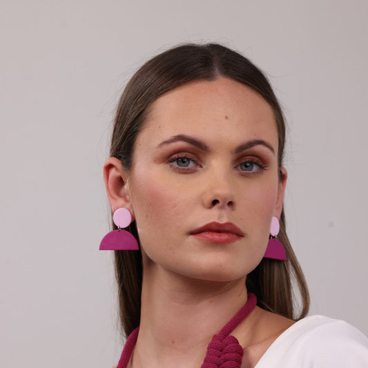 Woman wearing pink earrings and a matching necklace against a plain background