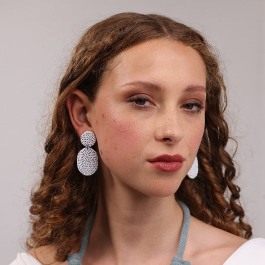 Woman wearing white earrings with a black speckled, against a neutral background.