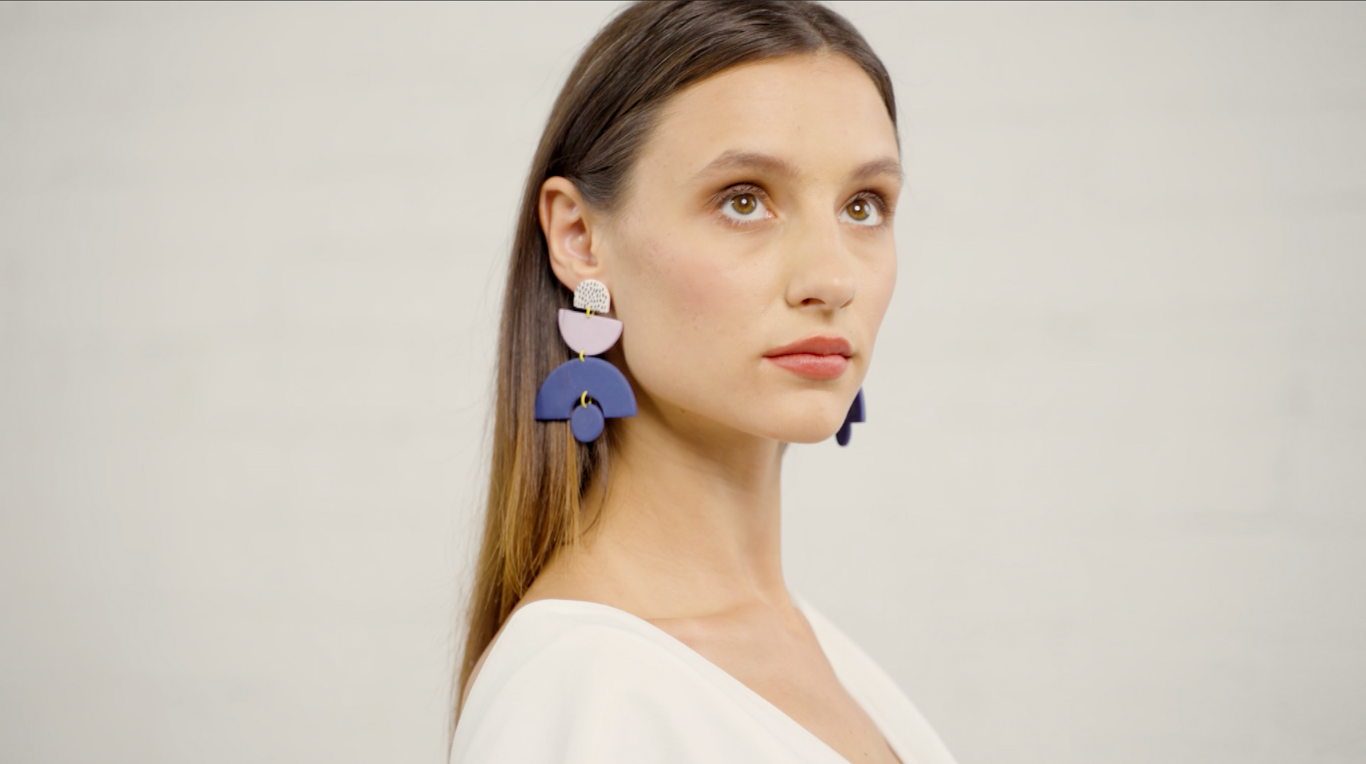 Load video: A model wearing a large pair of navy, lavender and white statement earrings.