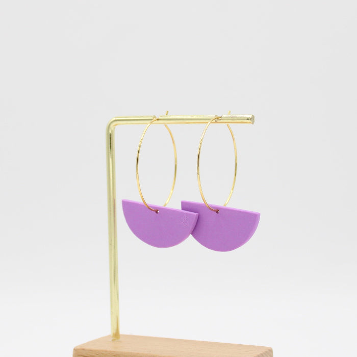 Purple semicircle hoop earrings hanging from gold hoops on a gold display stand with a wooden base, set against a plain white background.
