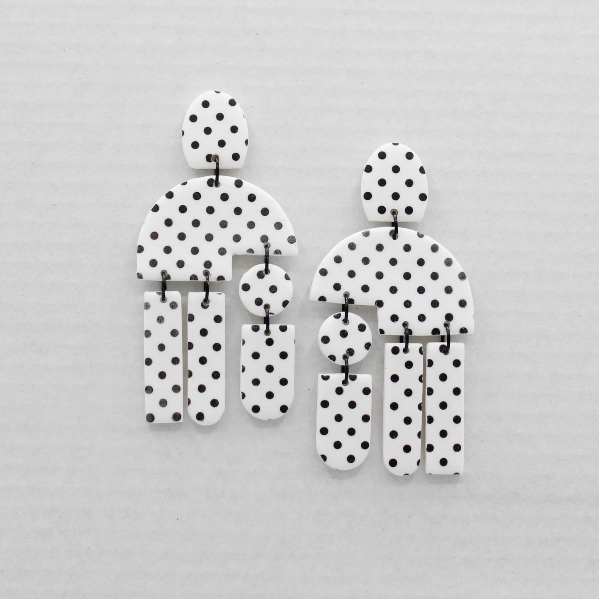 Two geometric shape earrings with a black and white polka dot pattern, displayed on a light gray textured background.